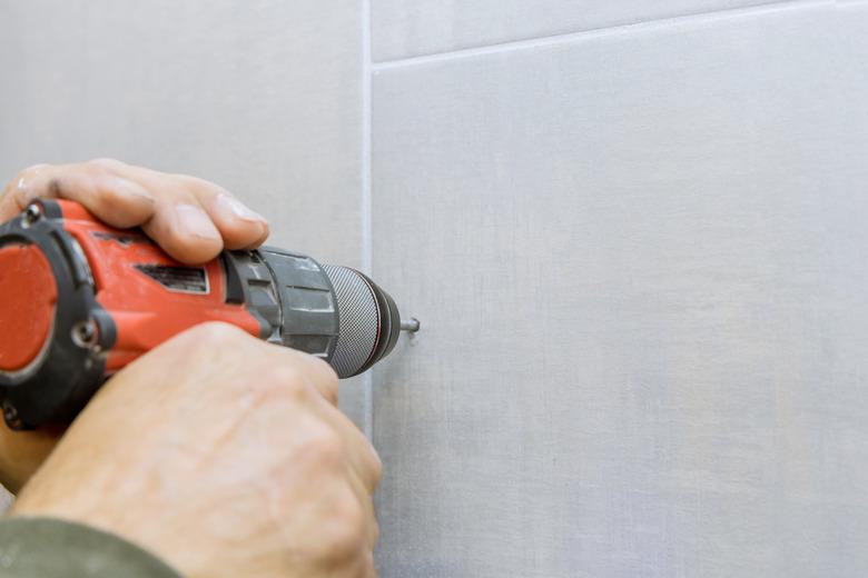 Closeup view of drilling hole in bathroom wall tile.