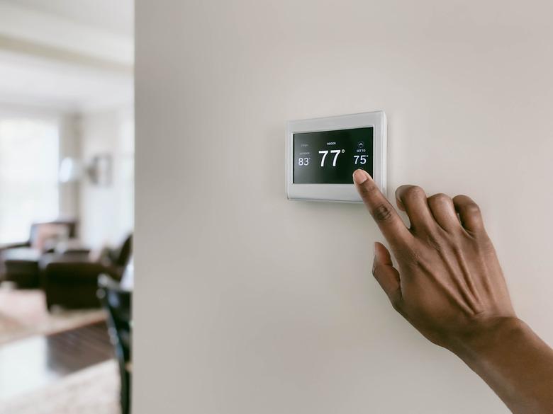 Woman adjusts white and black thermostat on white wall