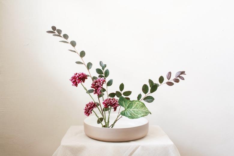 diy ikebana flower arrangement of burgundy flowers and long green leaves