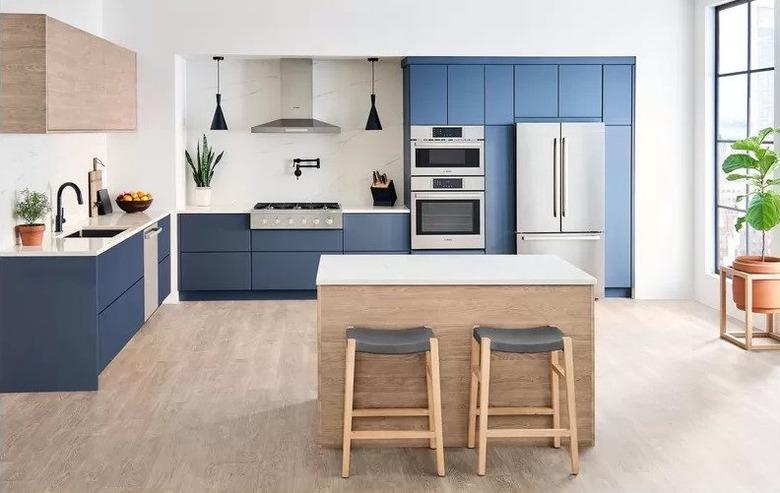 induction stove in Kitchen with blue cabinets, light wood kitchen island with light wood barstools, light wood floors, stainless steel appliances.