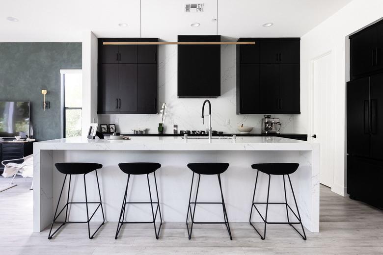 modern kitchen with white stone kitchen island, modern light fixture, black cabinets and black bar stools