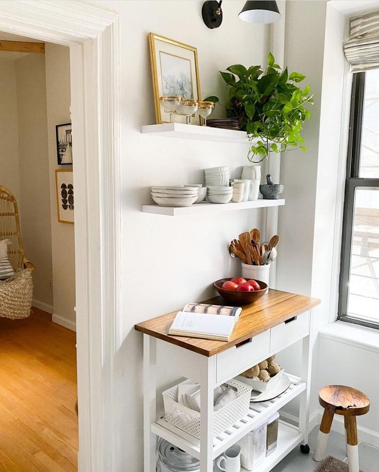 white kitchen cart with wood top alongside white floating shelves