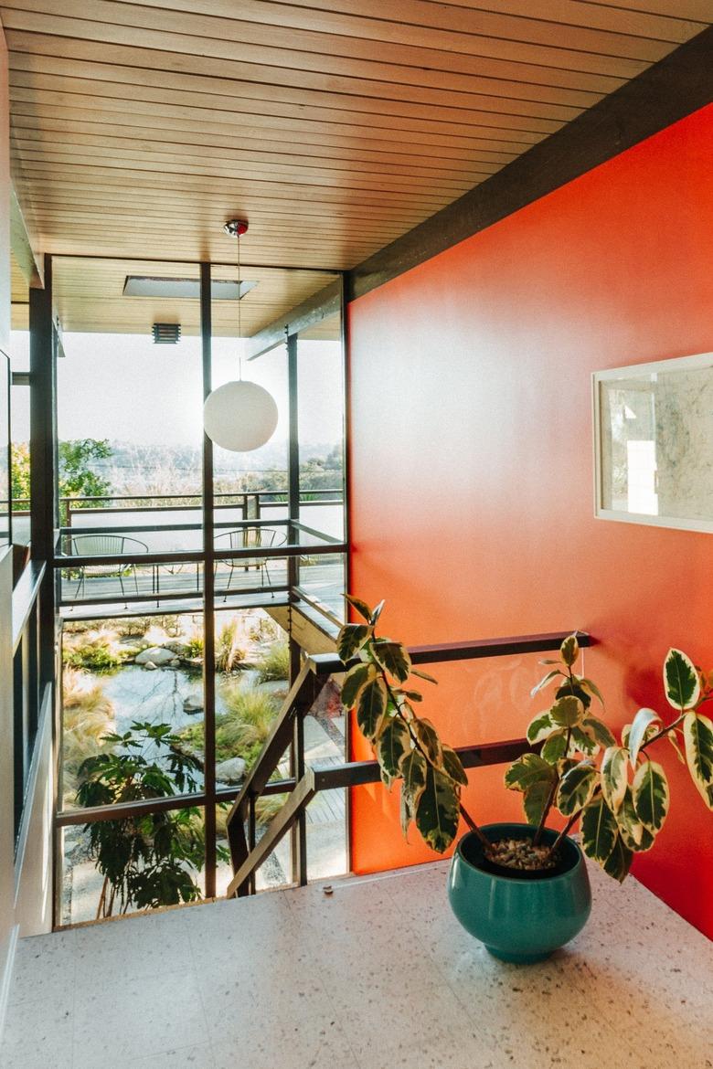 Midcentury staircase with bold burnt orange all and white globe pendant light