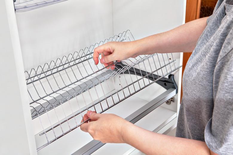 Installing wire dish rack for drying dishes inside kitchen cabinet.