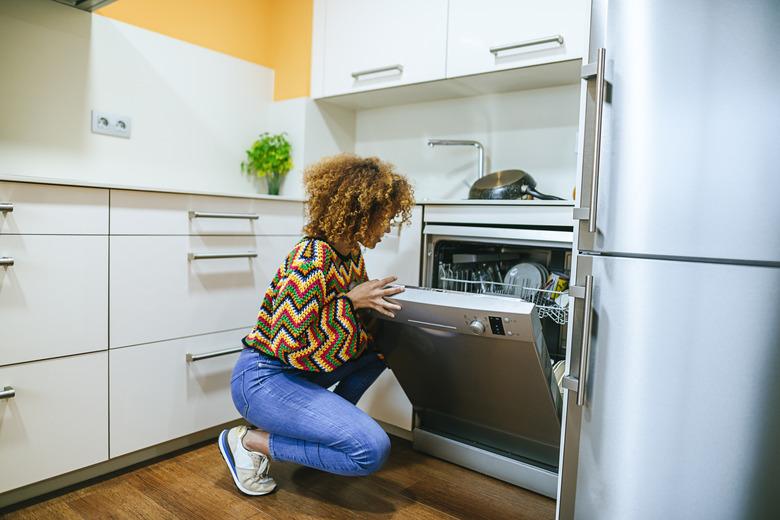 Young woman with curly opening the dishwasher in kitchen