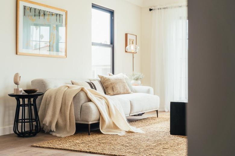 Living room couch with pillows and blanket, over sisal rug, glass and brass floor lamp, and black side table.