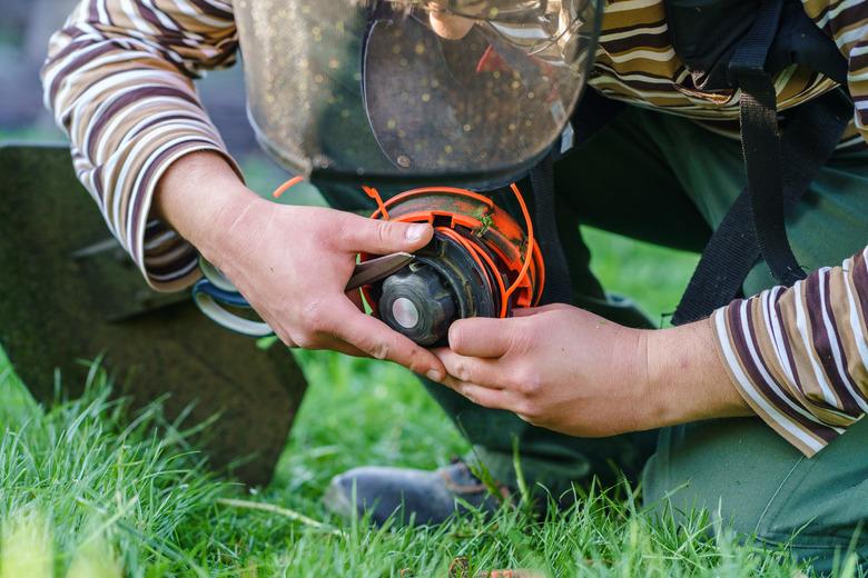 Close up on string trimmer head unknown caucasian man holding and repairing weed cutter replacing parts replacement in day on the field farmer or gardener