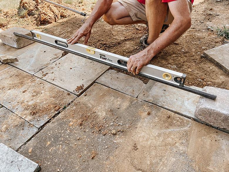 A construction worker using a level to measure between two concrete blocks and slate tiles