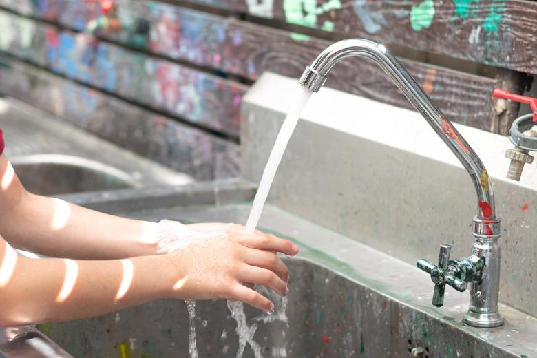 School children hand washing in running water faucet with mess up coloring paint in art class in school.