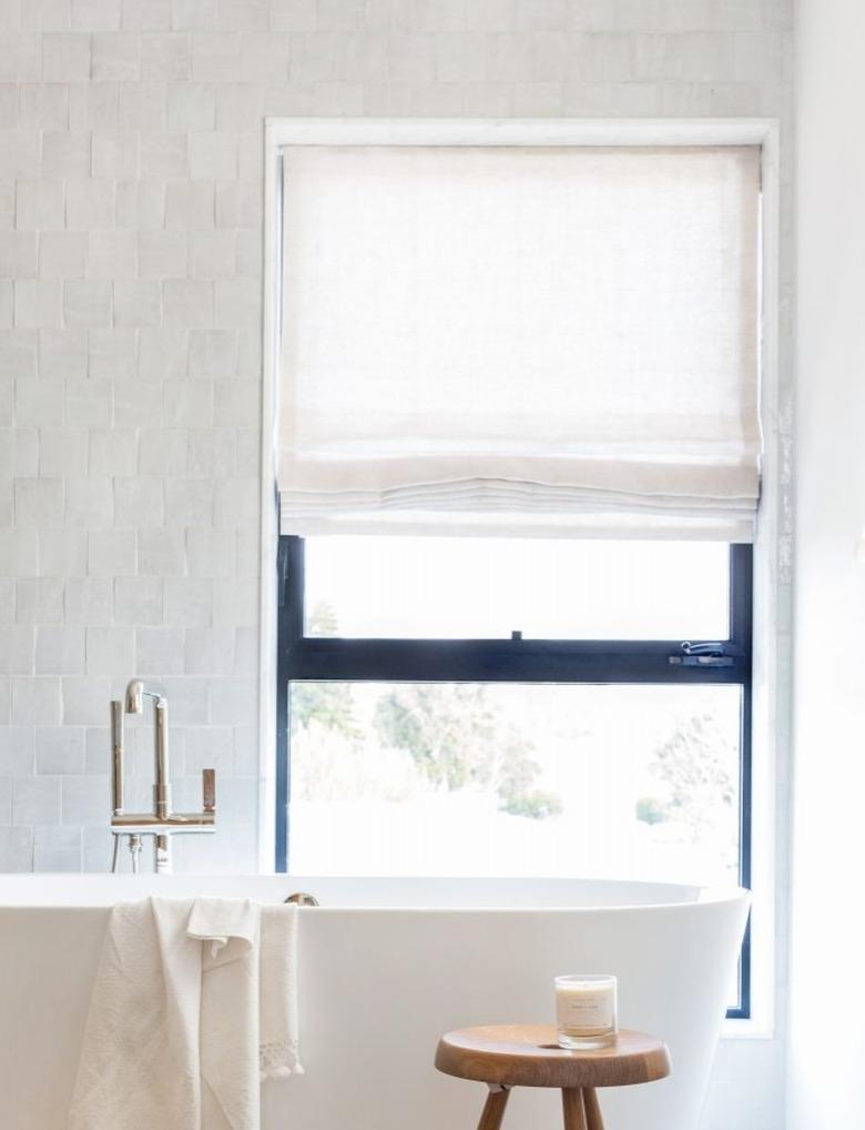 bathroom tub backsplash idea with zellige tile behind freestanding tub and window with Roman shade