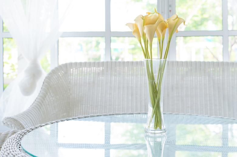 Yellow flower in vase on table and window sill background.