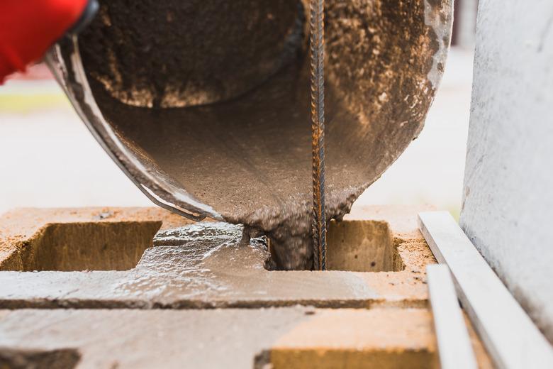 Cement slurry pouring from a bucket into the cells of a concrete block.