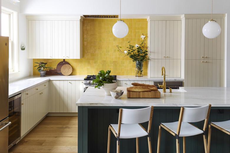 Mustard yellow tile kitchen backsplash with white cabinets and a green island