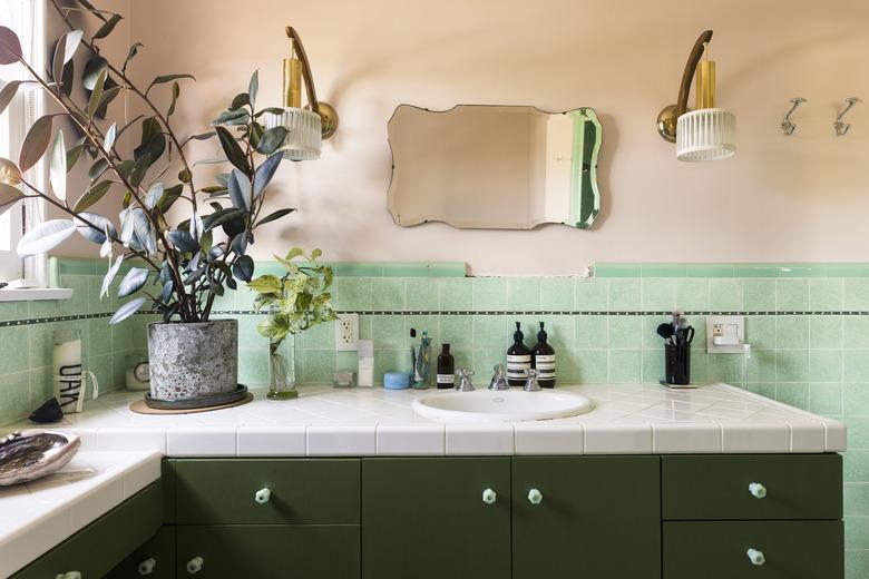 bathroom sink with green backsplash wall and small mirror