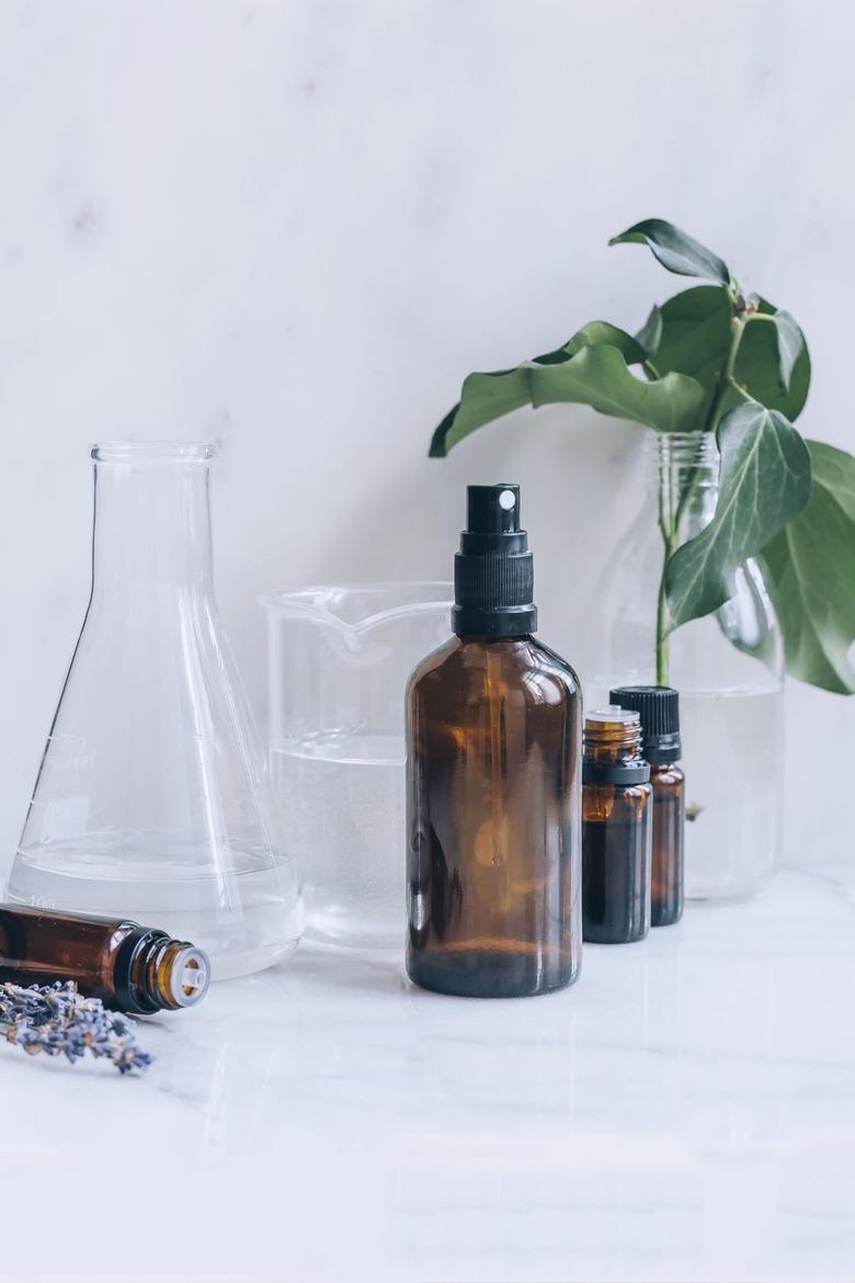 bottles of essential oil, lavender sprigs, glass beakers full of alcohol and water, and a spray bottle