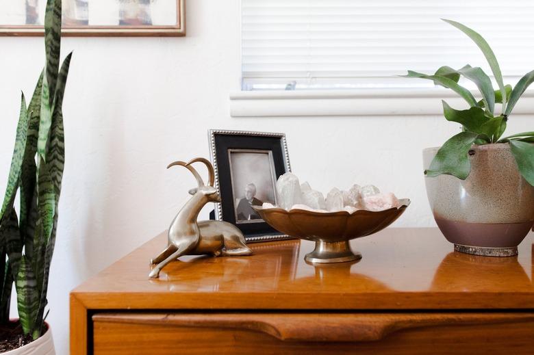 Wood credenza with a silver animal sculpture, framed family photo, a vintage silver bowl of crystals, and plants.