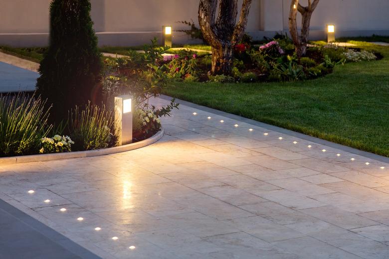 marble tile playground in the night backyard of mansion with flowerbeds and lawn with ground lamp and lighting in the warm light at dusk in the evening.