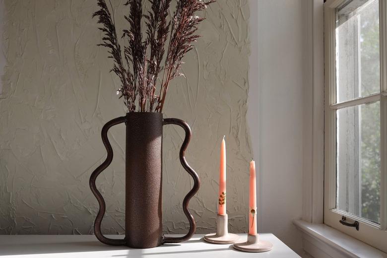 Dining table with a brown wavy vase of dried grass, and dried-pressed floral candlesticks.