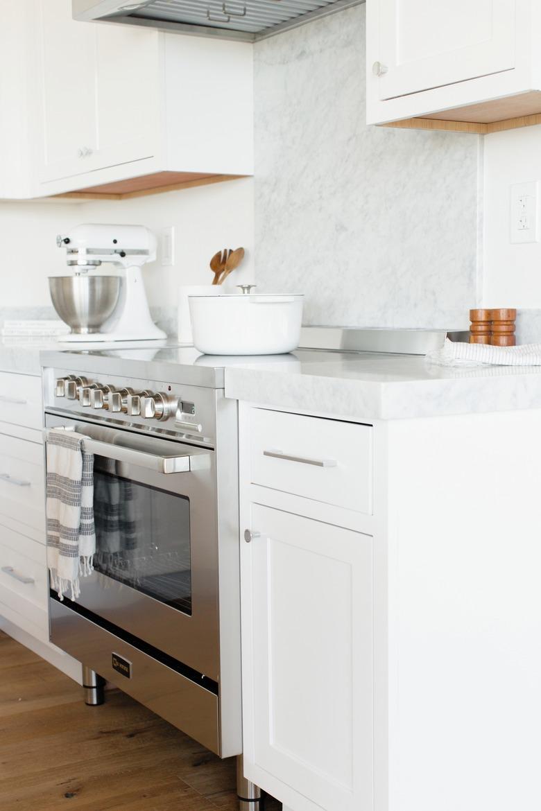 White kitchen cabinets with white marble backsplash, induction stove, mixer.