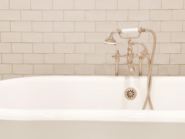 Old-fashioned polished nickel cross handle bathtub faucet & handheld sprayer with white enameled antique cast iron claw foot tub.