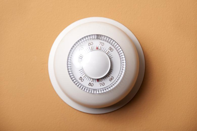 Round, white analog-dial thermostat on peach wall