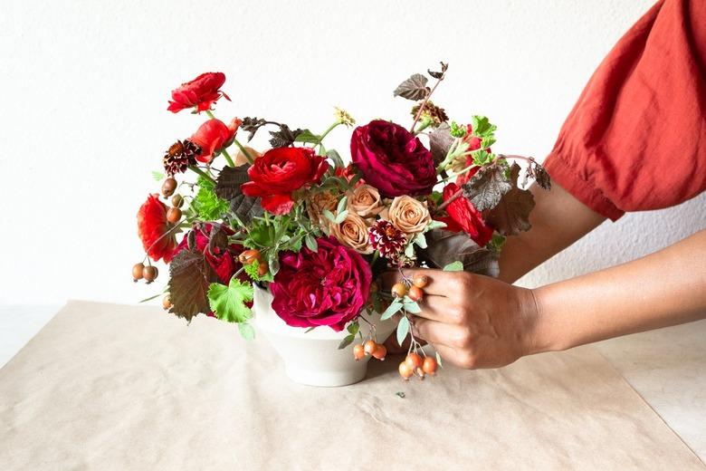 a diy floral centerpiece made of caramel roses and red flowers including ranunculus and zinnias