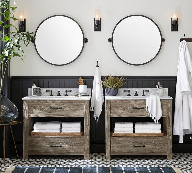 bathroom space with tiled floor, two wood vanities, two round mirrors, and three light sconces