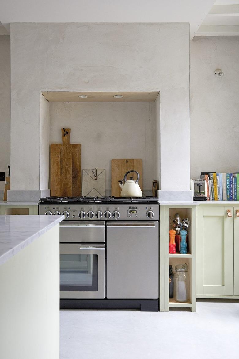 Neutral toned kitchen with soft green lower cabinets and bare plaster walls.