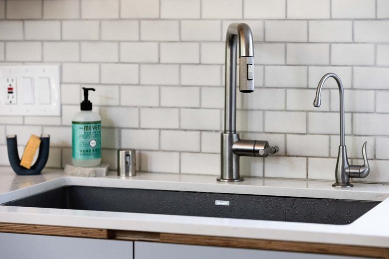 An undermount stainless steel sink in front of a white subway tile backsplash.