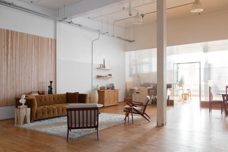 Minimalist living room with tufted brown leather couch, wood Modernist style chairs, white rug, and wood ridge accent wall.