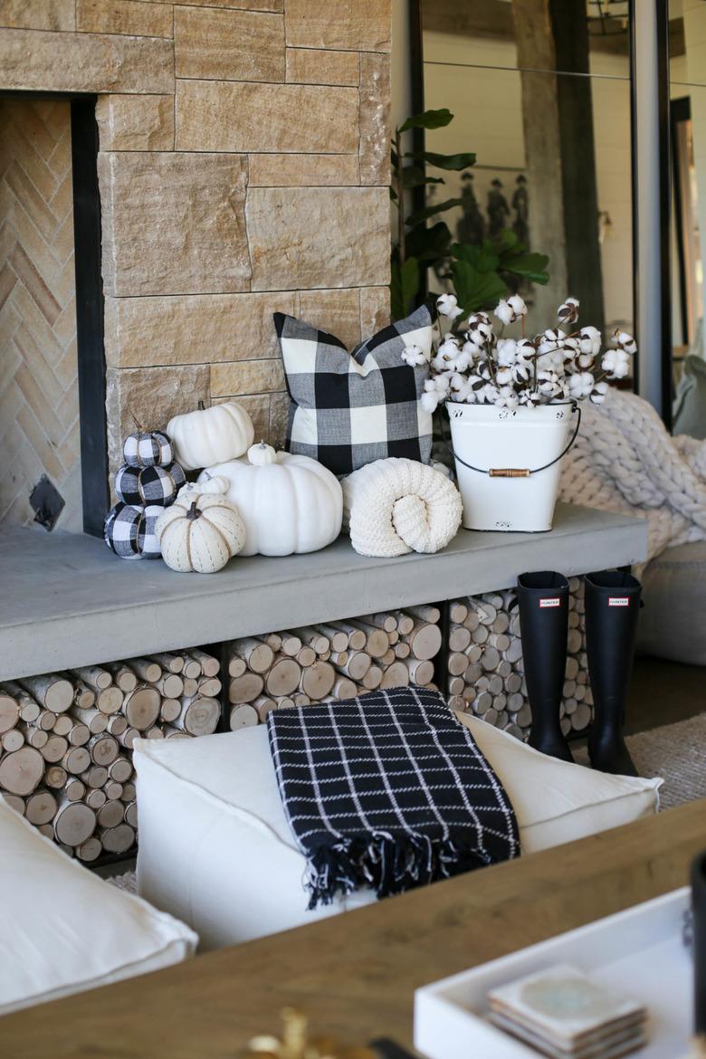 Rustic fall decor on fireplace with black and white plaid pillow and pumpkins