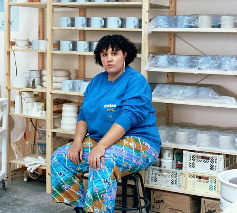 Sara Ekua Todd sitting on a stool in front of a shelf of mugs