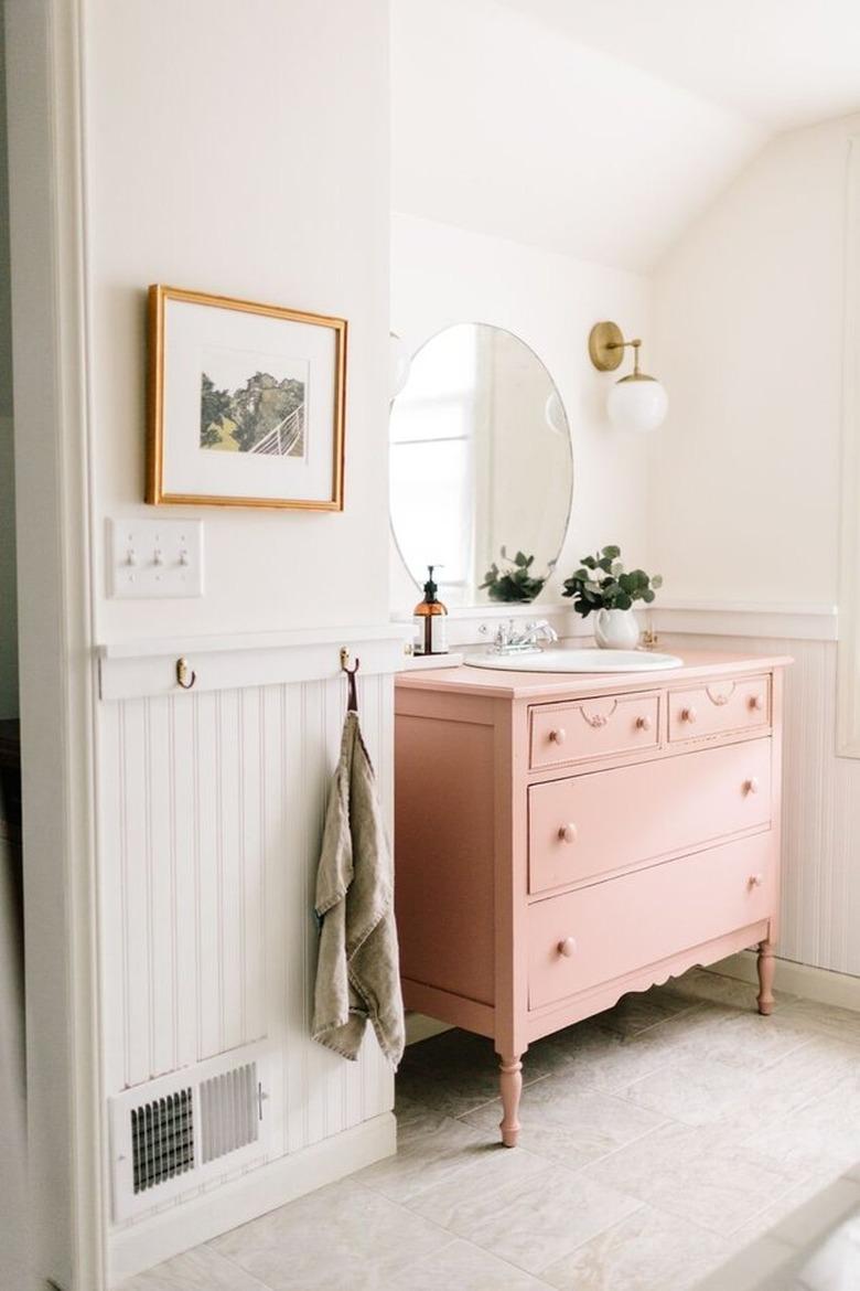 pink vintage dresser and self-rimming bathroom sink with round mirror and wall sconces