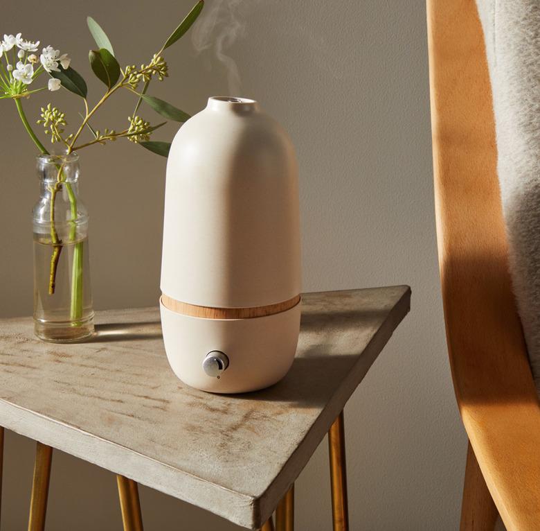 Beige diffuser, glass bud vase with flower, gray end table.