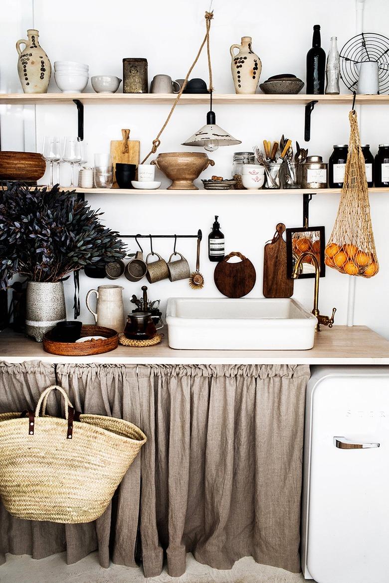 Rustic kitchen with open wood shelves and linen curtains under the counter.