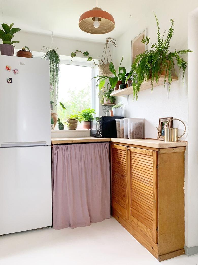 Bohemian kitchen with DIY cabinet curtain and hanging plants.