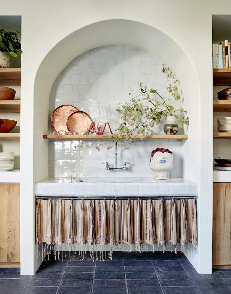 European style kitchen with blue tile floors and tasseled curtains under sink.