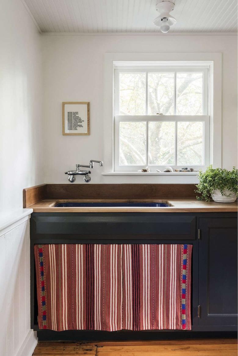 Kitchen with dark lower cabinets and vintage tapestry under the sink.