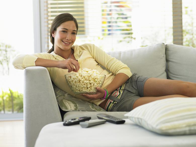 Teenage girl (14-16) watching television, holding popcorn, smiling