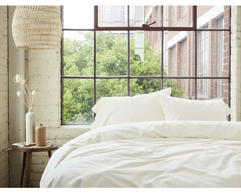 bedroom with small wood side table, woven lamp shade and bed with white sheets