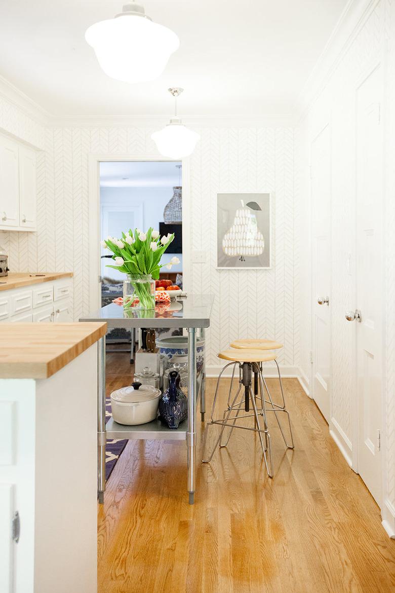 narrow stainless steel kitchen island in room with wood floors and white cabinets