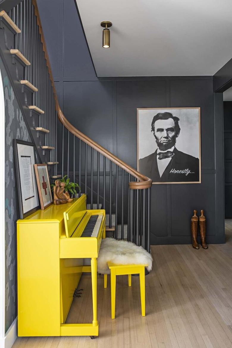 black stair railing with wood banister next to yellow piano