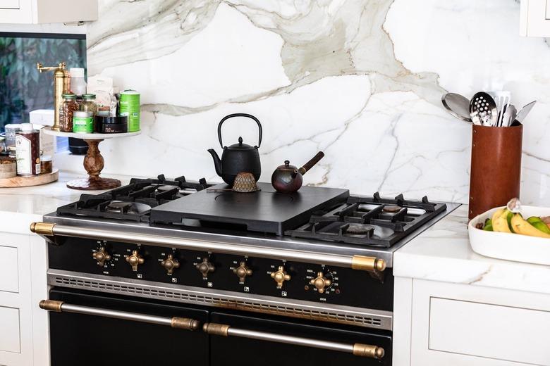 Stovetop with teapots in a kitchen with white countertops and granite backsplash