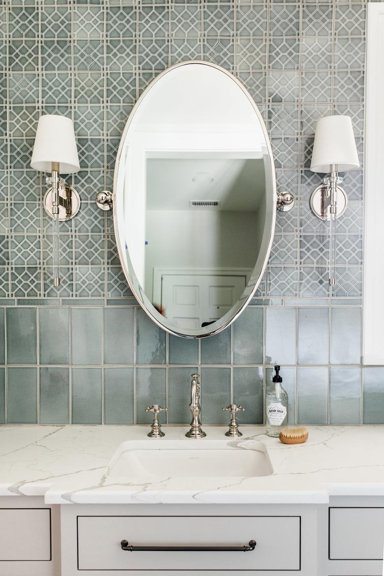 bathroom backsplash idea with different tile and oval mirror framed by wallsconces