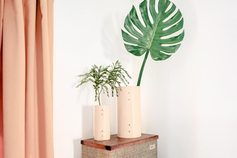 Beige leather vases with plants on side table next to peach curtains