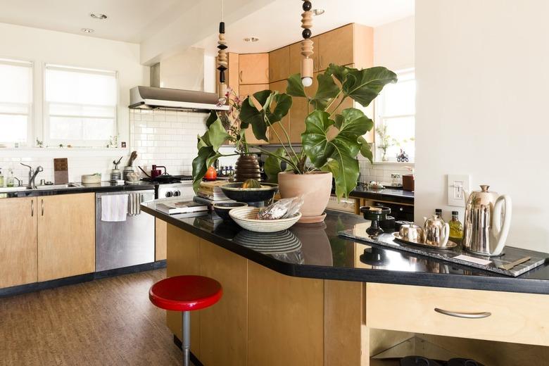 A red stool at a wood kitchen island with a black counter. Beaded pendant lights hang and a houseplant accent.