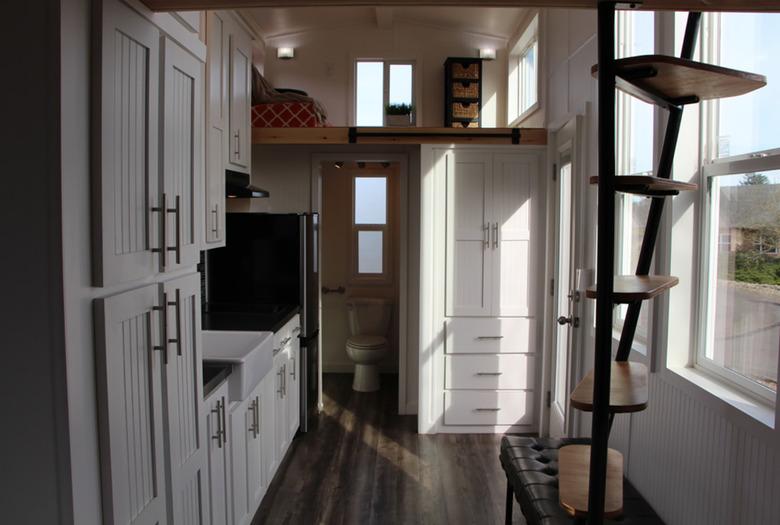 metal tiny house stairs in room with dark wood floors, wood, and white cabinets.