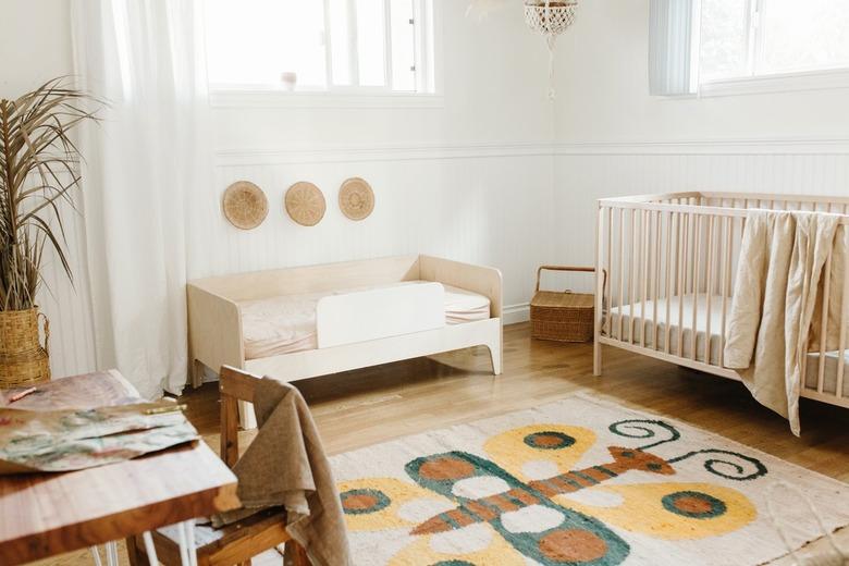 Children's nursery with wainscoting, wood floor, neutral crib and toddler bed