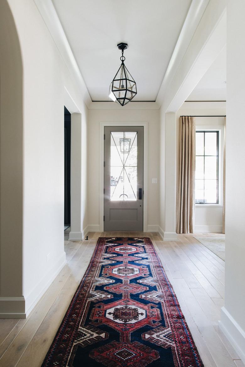 Entryway with glass pendant lamp, Oriental runner rug, wood floors.