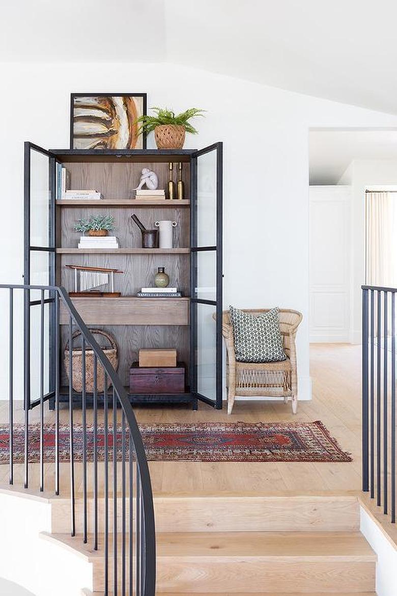 Hallway with shelving unit, objects, art, chair, rug.